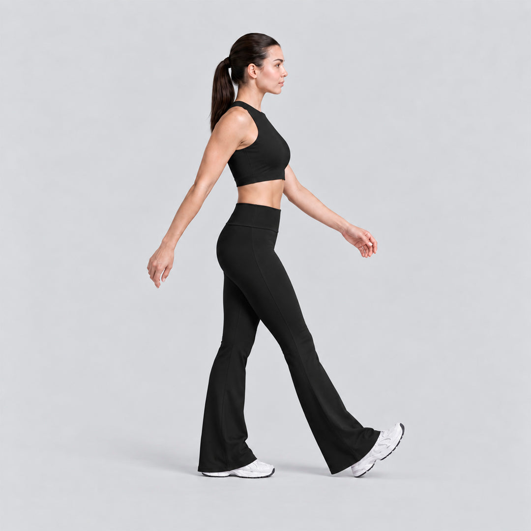 Conjunto deportivo negro visto de lado: top cropped y legging flare tiro alto.